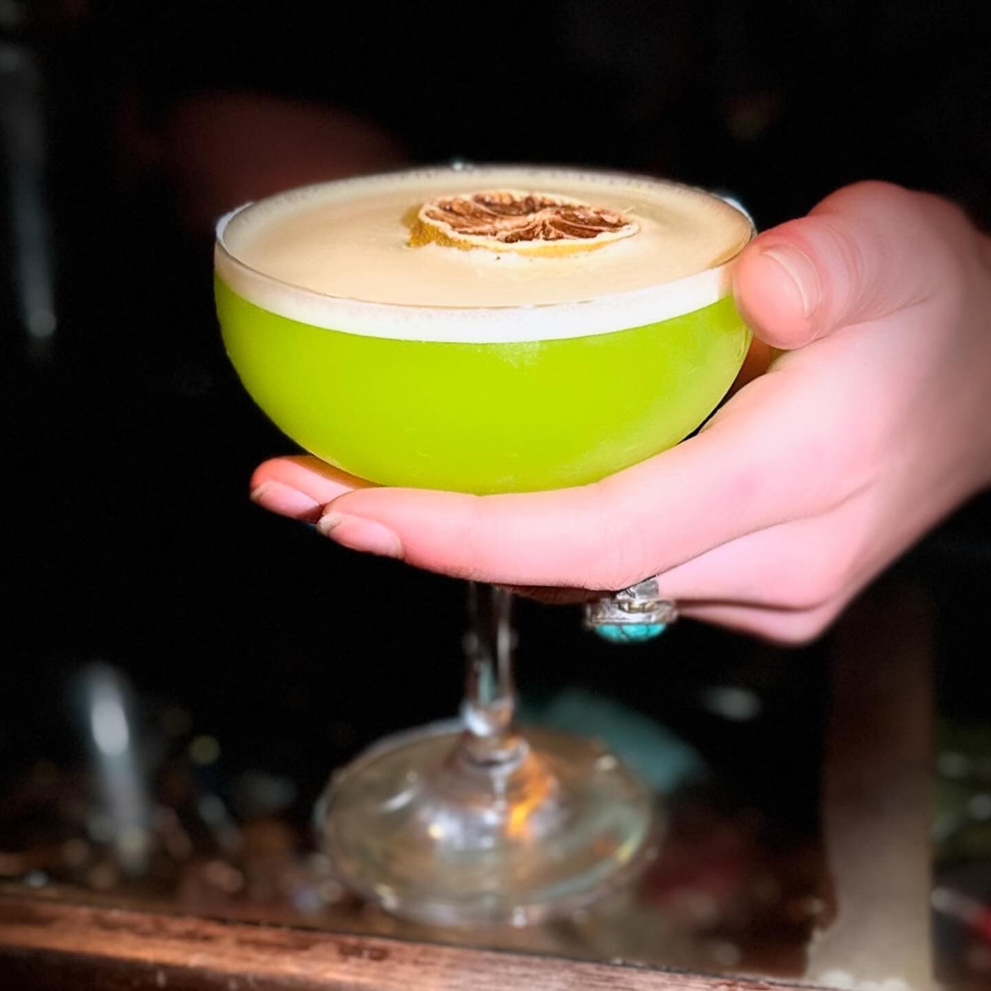 A foam-topped sour with charred citrus, lit dramatically from one side.